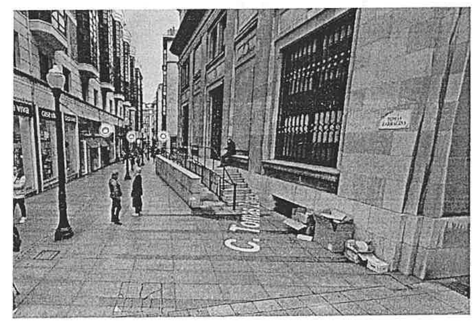 Fotografía de la calle peatonal junto a la fachada lateral de la Biblioteca Pública Jovellanos, con la acera y el acceso secundario del edificio.