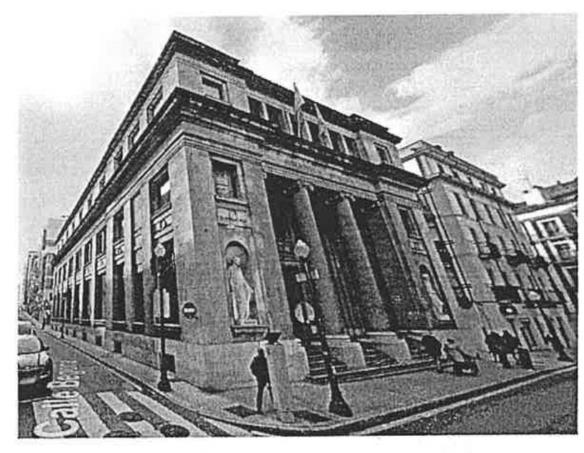 Fotografía exterior de la Biblioteca Pública Jovellanos de Gijón: edificio exento de varias plantas visto desde una esquina, con su fachada de columnas y la calle.